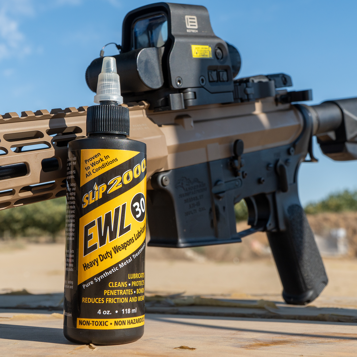 A Slip 2000 EWL30 bottle in front of a black and tar AR15 with an Eotech optic