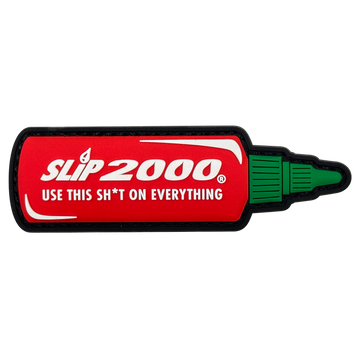 A PVC patch designed to look like a hot sauce bottle with the text 'SLIP 2000 USE THIS SH*T ON EVERYTHING' on a red background with the cap part of the design in green