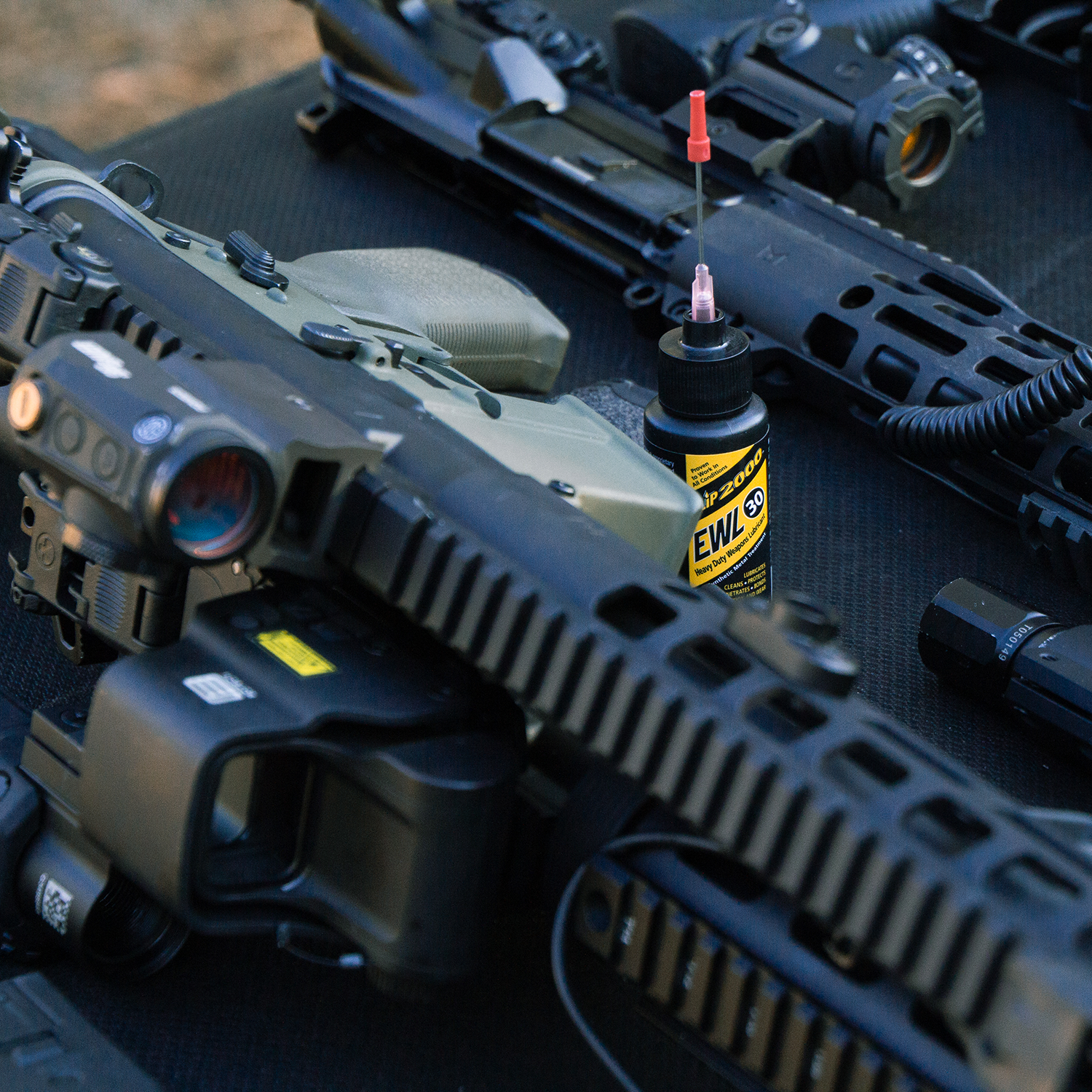A small Slip 2000 EWL30 bottle with a needle oiler next to a few AR15s