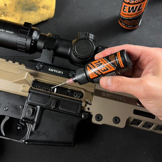 Orange Slip 2000 EWL bottle with a needle tip applying gun oil to an AR15 bolt carrier group on a workbench