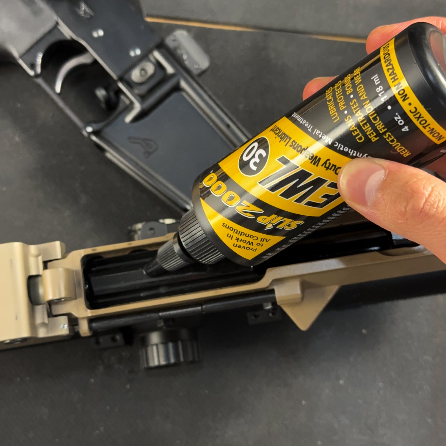 Slip 2000 EWL30 being used to lubricate the underside of an AR15 bolt carrier group on a black workbench