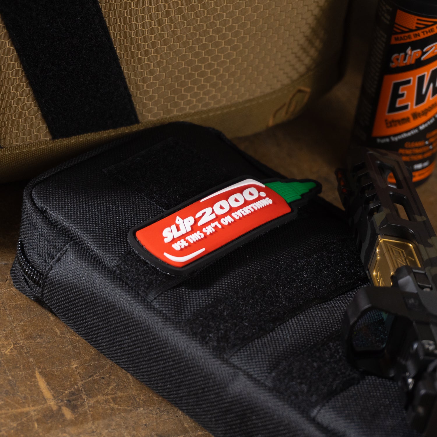 Red Slip 2000 hot sauce patch velcro'd on a cloth bag with a pistol slide resting near it.