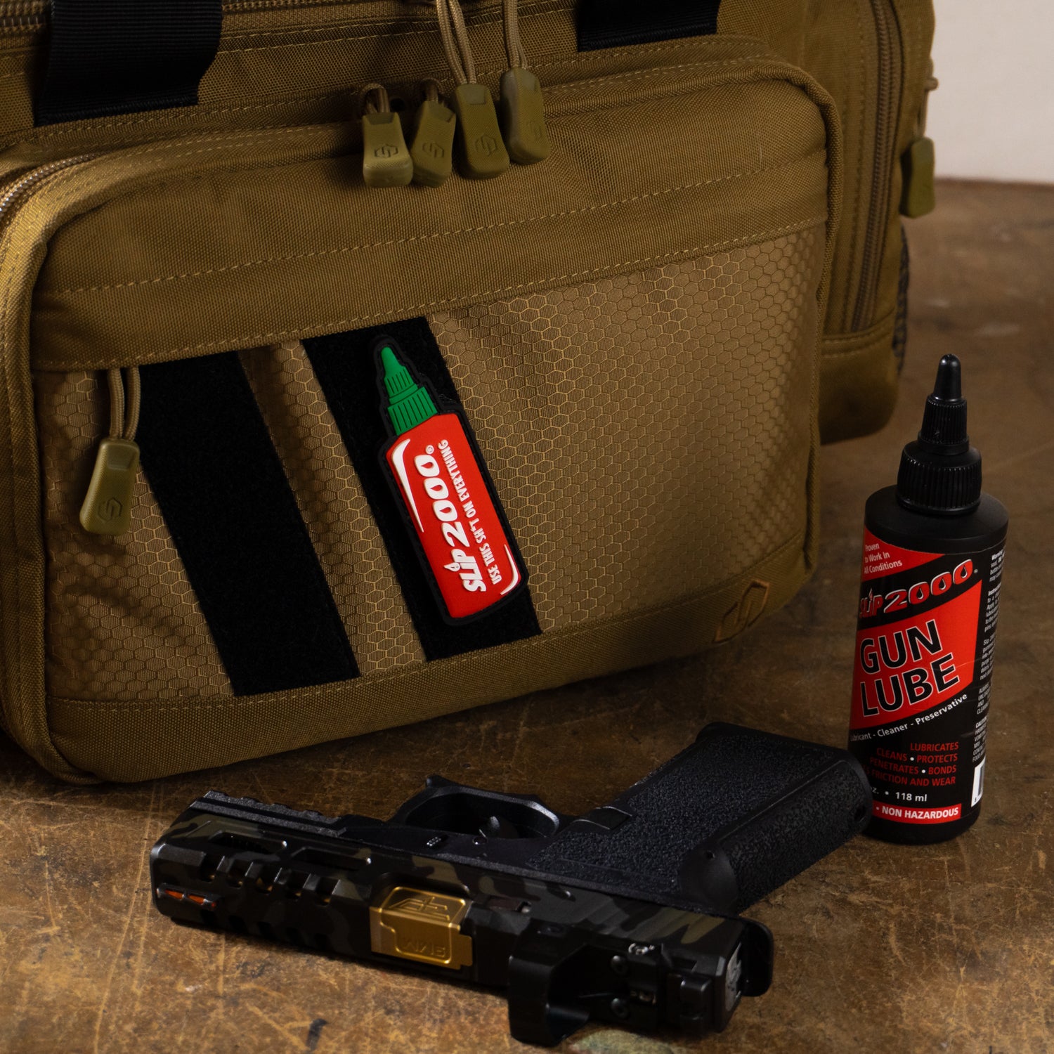 Slip 2000 Hot Sauce Patch on a tan pistol range bag with a bottle of Gun Lube and a pistol in front.