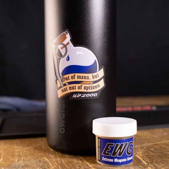 Sticker of a blue potion bottle with a grenade spoon saying "out of mana, but not out of options" on a black bottle with a tub of Slip 2000 EWG next to it.