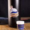 Sticker of a blue potion bottle with a grenade spoon saying "out of mana, but not out of options" on a black bottle with a tub of Slip 2000 EWG next to it.